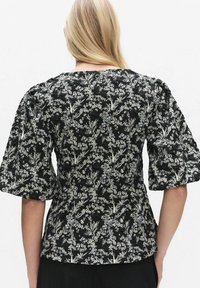 Svart blommig blus med puffärmar, texturerat tyg och ett mönster av ljusa blommor och blad över hela.