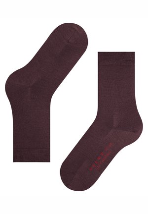 Paar dunkelbraune Knöchelsocken mit gerippten Bündchen, eine Socke liegt flach, die andere mit der Sohle nach oben, auf der rote Schrift auf weißem Hintergrund zu sehen ist.