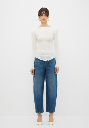 Hvid langærmet skjorte med samlet tekstur ved taljen, parret med lyseblå vidde jeans og cremefarvede højhælede sko.