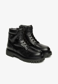 Schwarze Leder-Stiefeletten mit runder Spitze, glattem Obermaterial, gepolstertem Kragen und dicker Gummisohle mit einem strukturierten Profil.