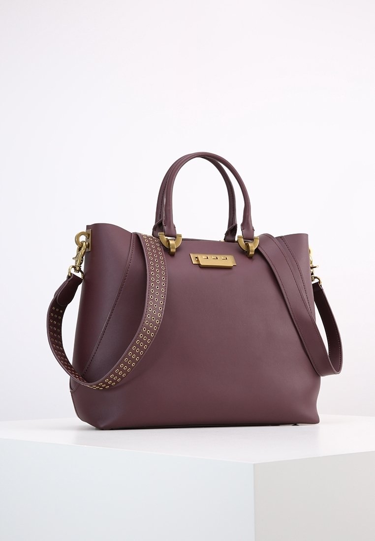 Borsa a mano in pelle bordeaux con hardware dorato, doppi manici e una tracolla perforata. Presenta una forma strutturata e una texture liscia.