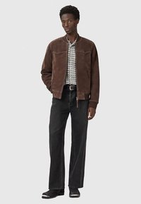 Jachetă maro din piele întoarsă cu fermoar frontal, cămașă gri cu carouri dedesubt, blugi negri cu picioare largi și pantofi negri cu accente argintii.