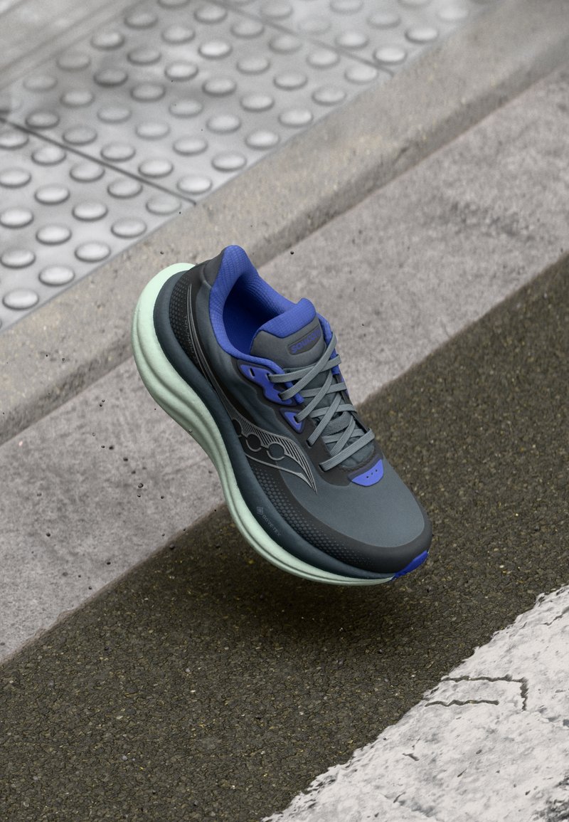 Sapatilha atlética cinza com sola verde, detalhes azuis e parte superior texturizada. Apresenta um design leve e um sistema de atacadores para um ajuste seguro.