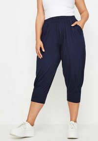 Mörkblå, lätta capribyxor med elastisk midja, sidofickor och samlad detalj vid fållen, kombinerat med vita sneakers.