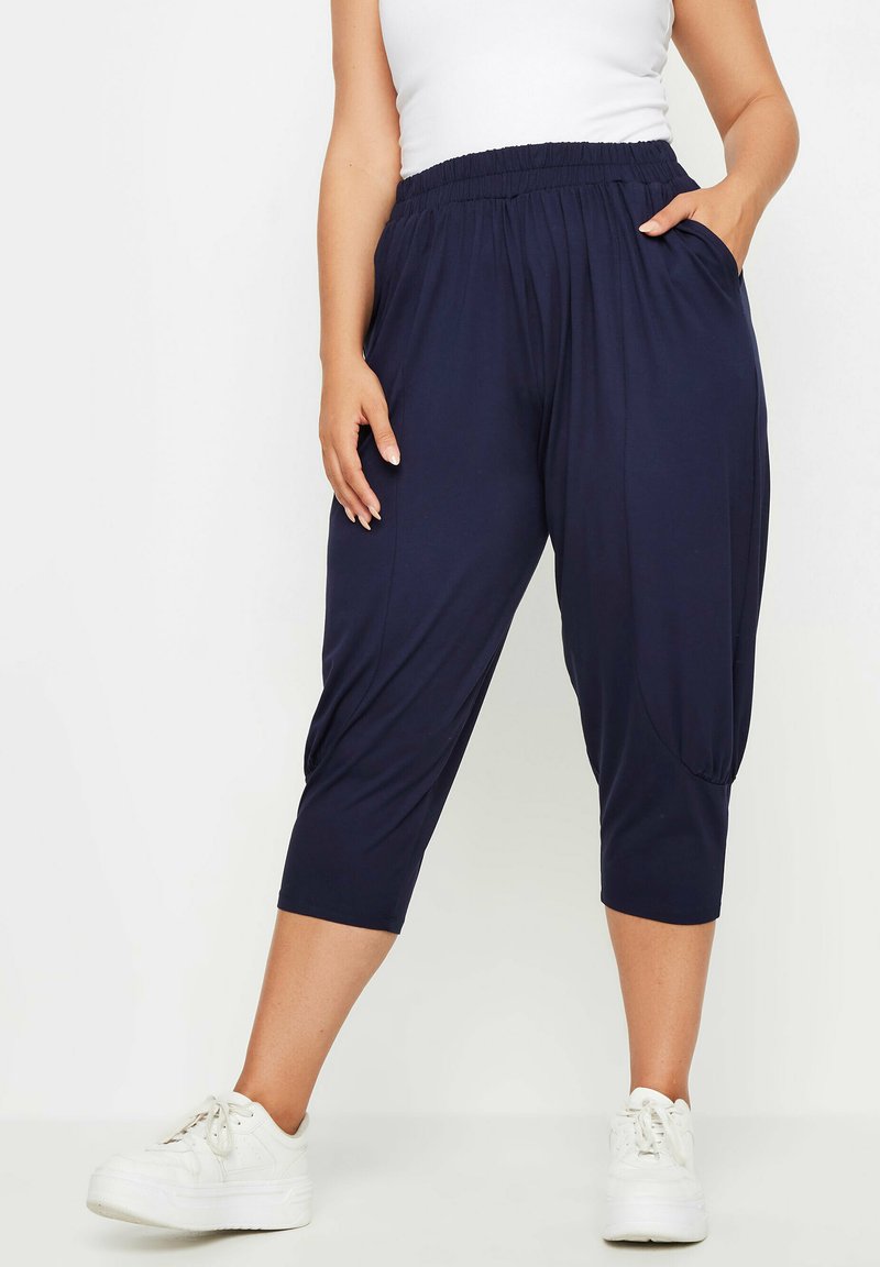 Mörkblå, lätta capribyxor med elastisk midja, sidofickor och samlad detalj vid fållen, kombinerat med vita sneakers.