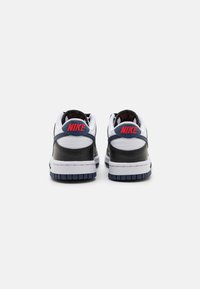 Nike sportiniai bateliai su balta tekstiline viršutine dalimi, juodais odiniais akcentais ir tamsiai mėlynais detalėmis. Kulkšnies vietoje yra raudonas logotipas ir struktūrizuota padas.