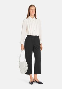 Weißes Hemd mit vertikalen Streifen, schwarze elastische Bundhose, weiße Fransenhandtasche und schwarze spitze Ballerinas.
