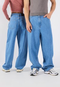 Jeans de ganga de perna larga em azul claro, com um corte relaxado, apresentando cinco bolsos e detalhes de costura discretos. Tecido texturizado com um acabamento suave.