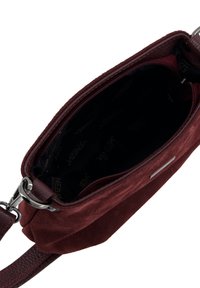 Zamszowa torebka w kolorze burgundowym z gładką skórzaną lamówką, zamkiem błyskawicznym i subtelnym oznaczeniem wewnątrz. Wnętrze wyłożone jest jednolitym czarnym materiałem.