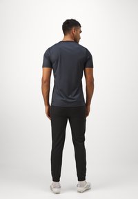Sportoutfit bestaande uit een aansluitend donkergrijs T-shirt met korte mouwen, zwarte broek en witte voetbalschoenen met zilveren accenten.