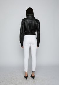 Chaqueta corta de cuero negro con cuello y mangas largas, combinada con jeans blancos ajustados y sandalias negras de tacón alto.