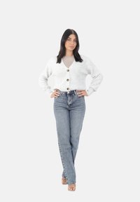 Grå, ribbad kofta med stora knappar, kombinerad med högmidjade blå jeans. En enkel beige topp under, bärs med sandaler med genomskinlig klack.