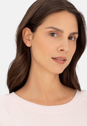Orecchini a bottone rotondi in argento, design semplice, su un maglione rosa chiaro a girocollo. Texture liscia, piccole dimensioni e lucentezza sottile.