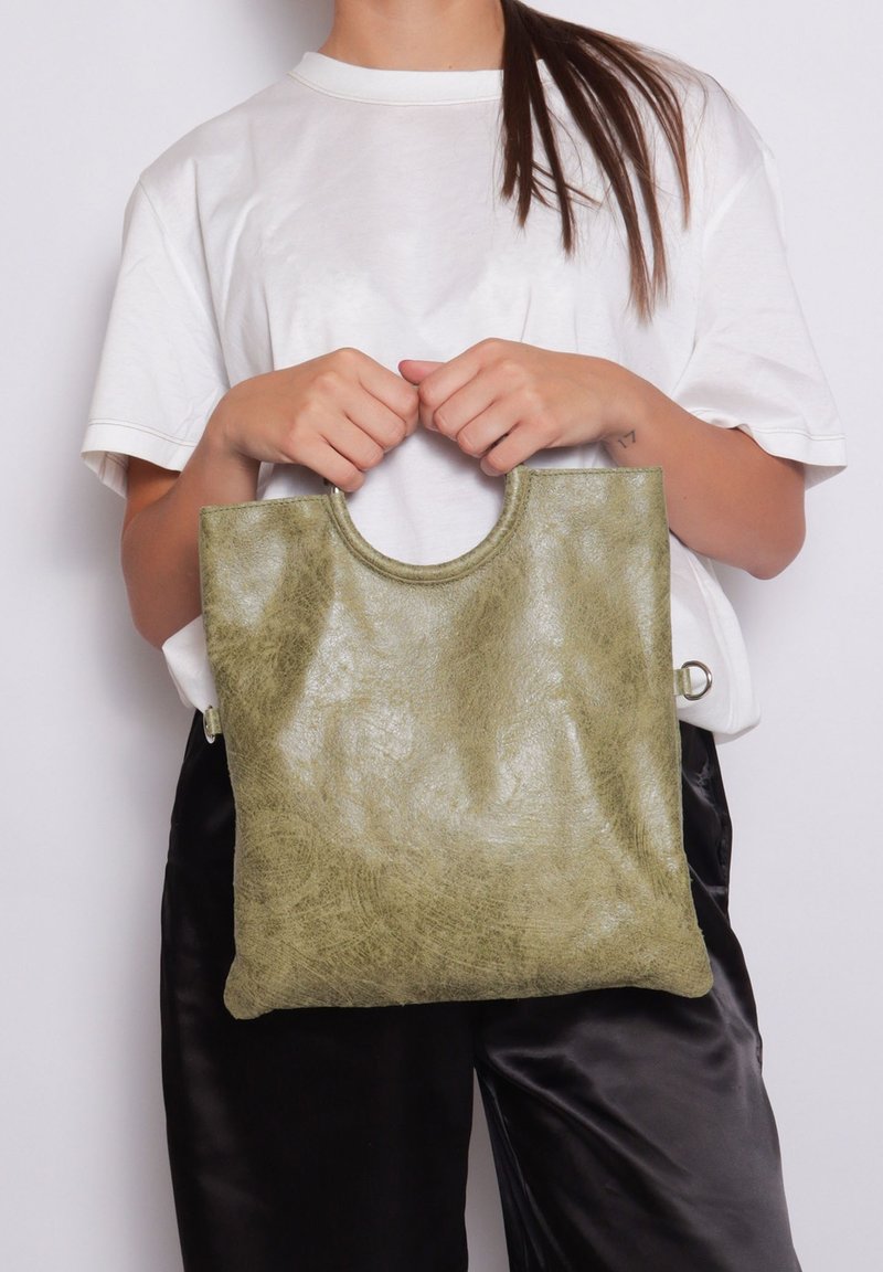 Groene, getextureerde tote bag met een ronde handgreep en ritsdetails, gemaakt van een zacht materiaal, weergegeven tegen een neutrale achtergrond.