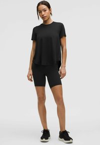 Zwarte sportieve t-shirt met korte mouwen, gecombineerd met zwarte fietsbroek. Soepele textuur, relaxte pasvorm en aangevuld met zwarte sneakers.