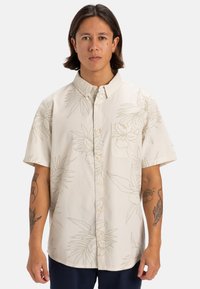 Camicia a maniche corte in crema con un motivo a contorni botanici, chiusura a bottoni e taschino sul petto. Realizzata in tessuto leggero.