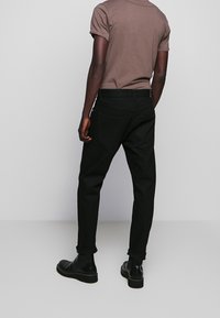 Jeans de mezclilla negra con fit ajustado, que presentan los puños enrollados, bolsillos traseros y un cinturón. Combinados con una camisa marrón de mangas cortas.