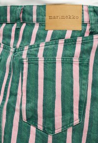 Πίσω τσέπη πράσινου και ροζ παντελονιού με κάθετες ρίγες, με ραμμένη ταμπέλα από ταμπά δέρμα που γράφει «marimekko».