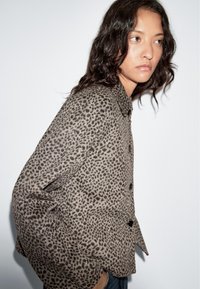 Brown leopard-print button-up jacket with a relaxed fit, featuring a collar and black buttons, made from soft, textured fabric.