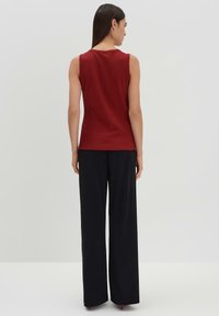 Top rosso senza maniche con una texture a coste, abbinato a pantaloni neri a gamba larga. L'outfit presenta un design pulito e minimalista.