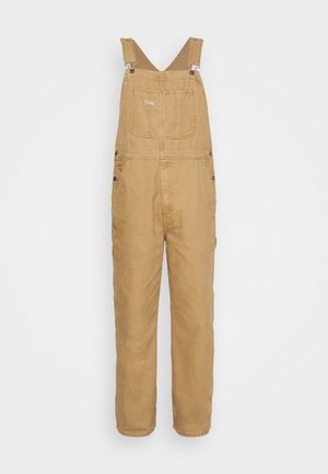 Salopette de travail en coton couleur tan, avec des bretelles réglables, une poche poitrine avant et des fermetures à boutons sur les côtés.