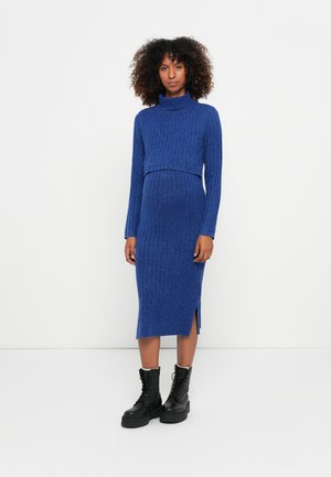 Blue ribbed knit dress with a turtleneck and long sleeves, featuring a fitted waist and side slit, worn with black lace-up boots.