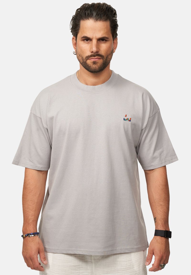 Helles graues T-Shirt aus Baumwolle mit relaxed Fit, kurzen Ärmeln und einem kleinen bunten Logo auf der Brust, mit einer weichen Textur.