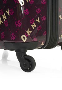 Maleta rígida de color púrpura oscuro con un acabado brillante, que presenta un patrón de logotipos en rosa y dorado y cuatro ruedas giratorias negras.