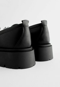 Zwarte leren schoenen met een ronde neus, opvallende stiksels en een dikke platformzool. Glad oppervlak en een korte trekband aan de hak.