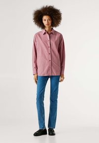 Camisa de botones de manga larga a rayas rojas y blancas, combinada con jeans azules y mocasines negros. Cuello sencillo y diseño recto.