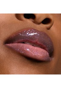 Prodotto per labbra lucido con una sfumatura che va dal rosa traslucido a un viola più scuro, caratterizzato da piccole particelle di glitter e una texture liscia e riflettente.