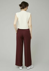 Haut sans manches blanc texturé associé à un pantalon large bordeaux. La tenue est complétée par des baskets blanches et des accessoires minimalistes.