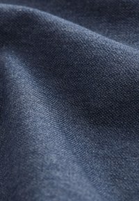 Detailní záběr tmavě modré pletené látky zobrazující texturovaný vzor pletení a jemné záhyby materiálu.