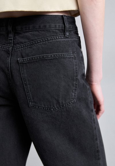 Black denim jeans with a straight cut, featuring a back pocket and subtle stitching details. Fabric has a soft texture and minimal sheen.