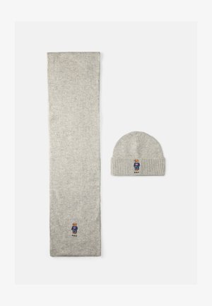 Lys grå strikket skjerf med ribbkanter og en liten bjørnelogo. Follows av en matchende grå lue med den samme logoen.