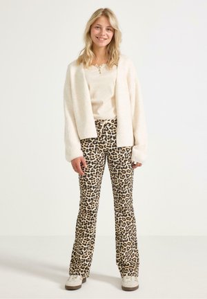 Cardigan bianco e morbido sopra un top beige, abbinato a pantaloni a zampa d'elefante con stampa leopardata. Sneakers casual completano l'outfit. Sfondo chiaro.
