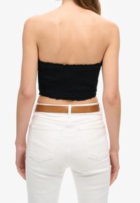 Woman wearing a black strapless top and white pants with a brown belt, shown from the back against a white background.