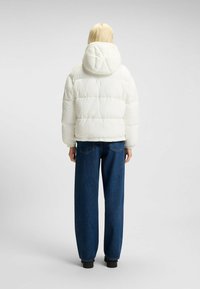 Vit puffjacka med huva, med kviltad design och elastiska ärmslut, kombinerad med lösa blå denimjeans och svarta skor.