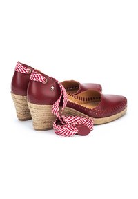 Chaussures à talon compensé en cuir rouge avec un talon en jute tressé, des bords festonnés et des lacets à motifs rouge et blanc. Coutures détaillées autour des orteils.