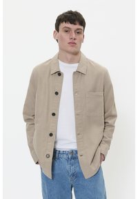 Jachetă bej cu nasturi, cu guler, un buzunar pe piept și nasturi negri. Purtați-o peste un tricou alb și asortați-o cu pantaloni din denim albastru.