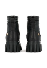 Botas de combate de cuero negro con un puño acolchado, suela de goma gruesa y un acento de logo dorado en el costado. Presenta un acabado texturizado.