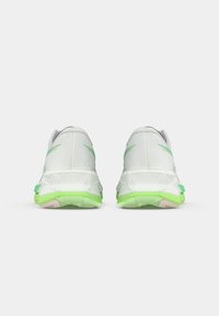 White running shoes with a textured upper, featuring green accents on the sole and heel. The design is athletic and lightweight.
