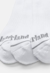 Bílé bavlněné ponožky s žebrovaným designem a šedým logem na straně. Ponožky mají měkkou texturu a standardní délku do kotníků.