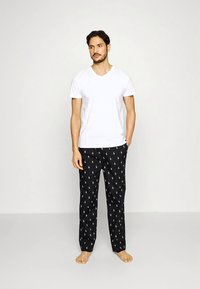 Witte V-hals T-shirt gecombineerd met zwarte pyjamabroek met een herhalend wit logo patroon. Materiaal lijkt zacht en heeft een relaxte pasvorm.