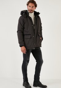 Dark gray padded jacket with a fur-lined hood, featuring front snap closure, two large pockets, and a water-resistant texture.