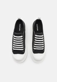 Schwarze Leinensneaker mit weißen Schnürsenkeln, einer dicken weißen Sohle und Zuglasche hinten. Steppnähte und Branding sind innen sichtbar.