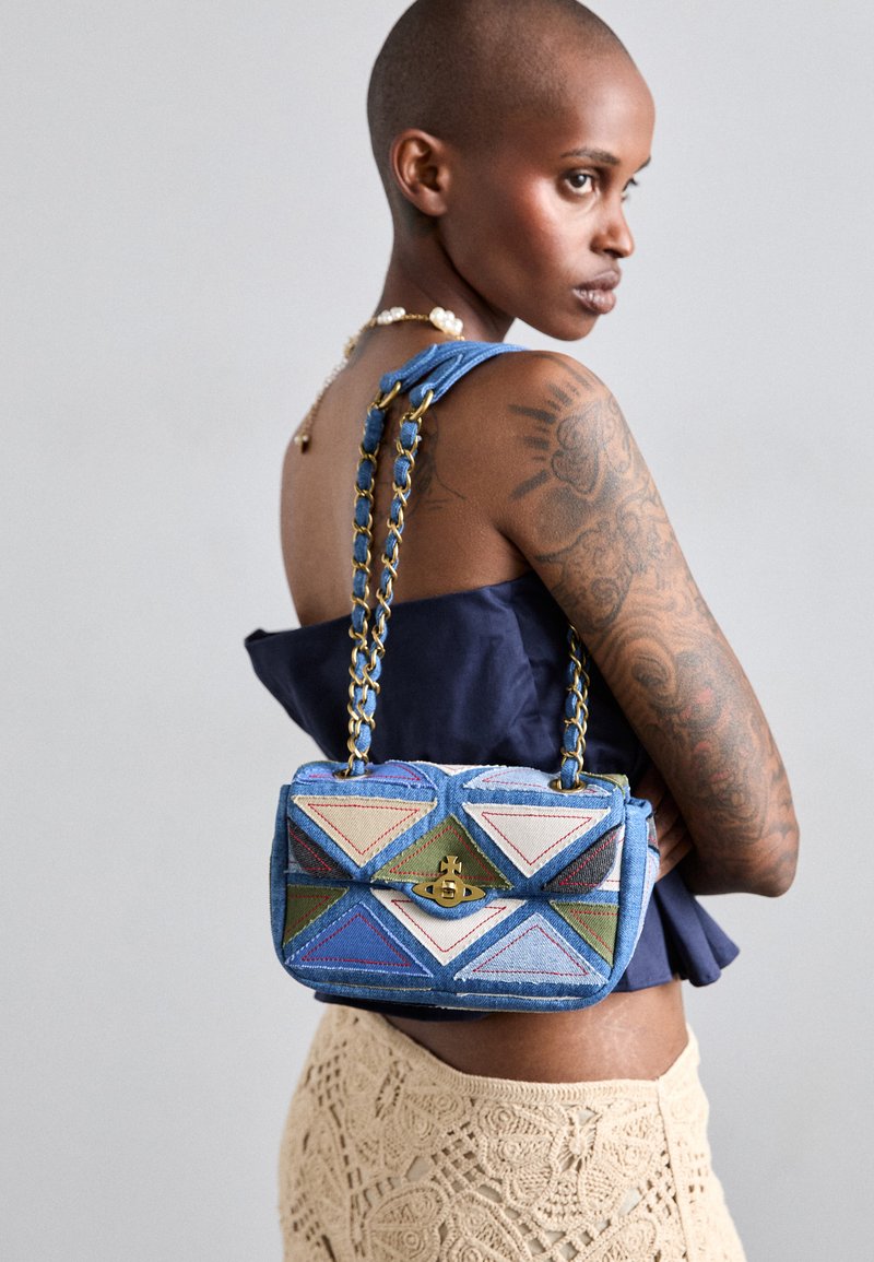 Borsa in denim blu con motivi geometrici triangolari in blu, verde e beige. Presenta una chiusura dorata e una tracolla a catena.