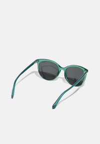 Ochelari de soare verzi transparenți cu lentile gri închise, design cat-eye, brațe subțiri cu accente metalice subtile și un finisaj lucios.