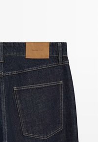 Dunkelblaue Jeans aus Denim mit einem Lederetikett "Massimo Dutti", das am hinteren Taillenbund eingenäht ist. Detaillierte Nähte an Taschen und Nähten.