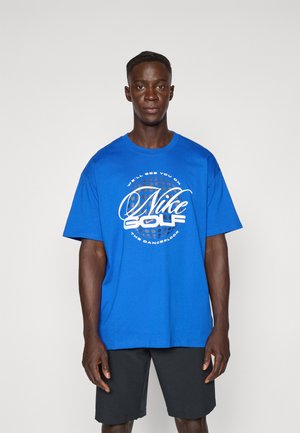 Blue cotton t-shirt with short sleeves, featuring a white graphic print that reads "Nike Golf" and a circular pattern in the center.